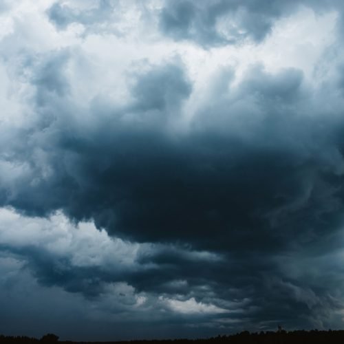Dramatic cloudscape. Sunny light through dark heavy thunderstorm clouds before rain. Overcast rainy bad weather. Storm warning. Natural blue background of cumulonimbus. Sunlight in stormy cloudy sky.
