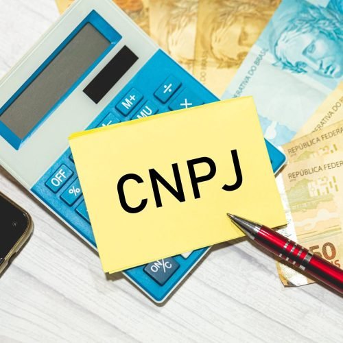 The acronym CNPJ for the National Register of Legal Entities in Brazil written on a piece of paper lying on top of a calculator. Brazilian Real banknotes in the composition. Brazilian economy.